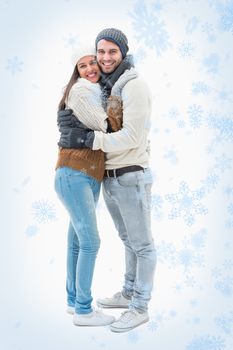 Attractive young couple in warm clothes hugging against snow falling