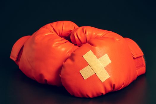 Red boxing gloves in the dark background. Adhesive plaster across each other on boxing gloves. The idea of getting hurt or combat losing business rivals. The idea of fighting giving up boxing.