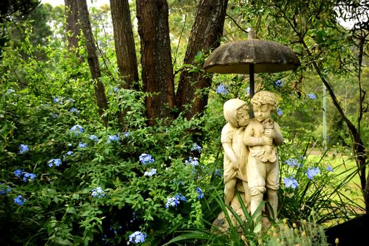 A statue of a young couple in a garden holding an umbrella