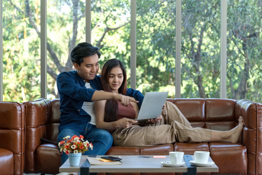 Young lovers spend time together on holidays in the living room. Both of them are interested in internet product information while the girl held laptop computer.