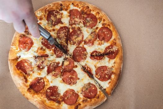 cropped male hand cuts pizza margarita with pepperoni with a special knife, closeup. Top view, copy space.