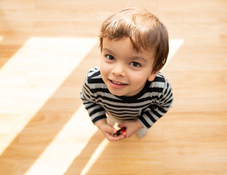 Toddler looking up and smiling at the camera in brightly sunlit room