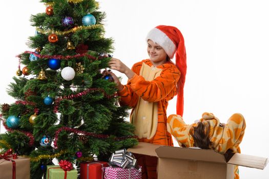 One girl hangs a ball on the Christmas tree, the other climbed into the box with her head