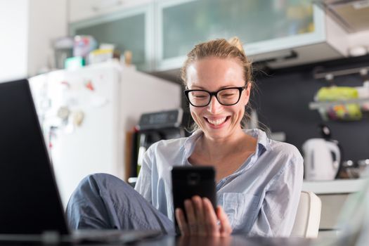 Stay at home and social distancing. Woman in her casual home clothing working remotly from kitchen dining table. Video chatting using social media with friend, family, business clients or partners.