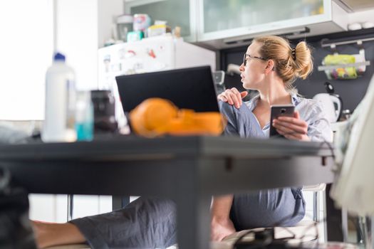 Stay at home and social distancing. Woman in her casual home clothing working remotly from kitchen dining table. Video chatting using social media with friend, family, business clients or partners.