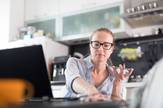 Stay at home and social distancing. Woman in her casual home clothing working remotly from her kitchen dining table in the morning. Video chatting with friend, family or business clients or partners.