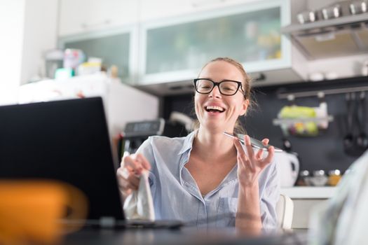 Stay at home and social distancing. Woman in her casual home clothing working remotly from kitchen dining table. Video chatting using social media with friend, family, business clients or partners.