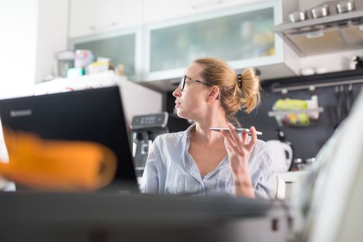 Stay at home and social distancing. Woman in her casual home clothing working remotly from her kitchen dining table in the morning. Video chatting with friend, family or business clients or partners.