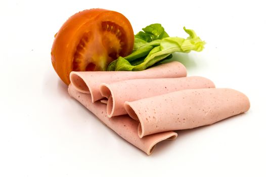 Slice of ham or Paris sausage on a white background with half a tomato and a salad leaf