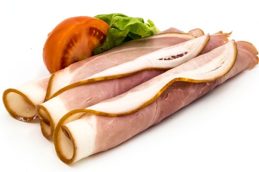 Slice of cooked ham on a white background with half a tomato and a salad leaf