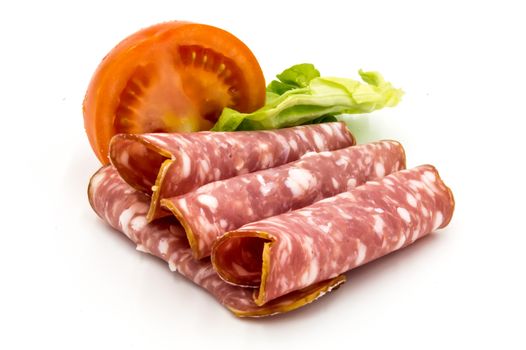 Slice of Gaumais sausage on a white background with half a tomato and a salad leaf