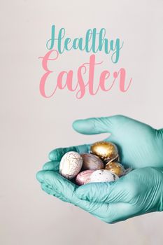 Hands in medical gloves holding modern painted easter eggs. Selective focus. Toned picture. Isolated. Healthy Easter text.