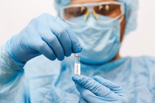 Close up of doctor hand holding vaccine. Medical equipment. A doctor wearing personal protective equipment including mask, goggle, and suit to protect COVID 19 coronavirus infection.