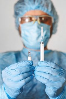 Close up of doctor hand holding vaccine. Medical equipment. A doctor wearing personal protective equipment including mask, goggle, and suit to protect COVID 19 coronavirus infection.