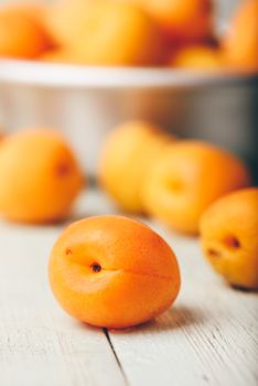 Mellow apricots over light wooden surface and metal bowl with fruits on background