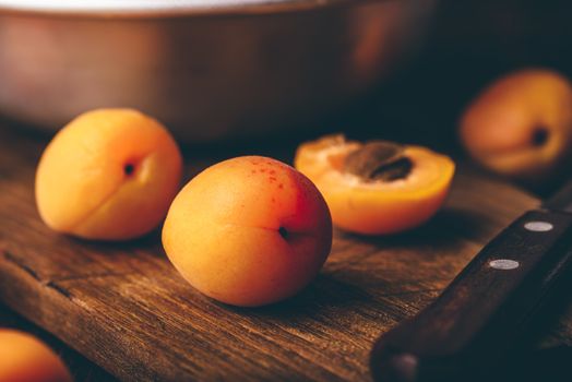 Mellow apricots with knife over old wooden cutting board and metal bowl with fruits