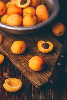 Mellow apricots with knife over old wooden cutting board and metal bowl with fruits