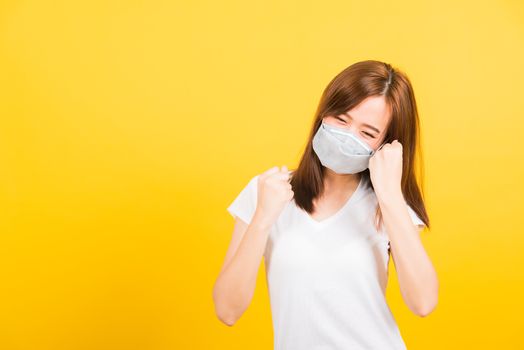 Portrait Asian beautiful happy young woman wearing face mask protects filter dust pm2.5, virus and air pollution her raise hands glad excited cheerful after recover from illness on yellow background