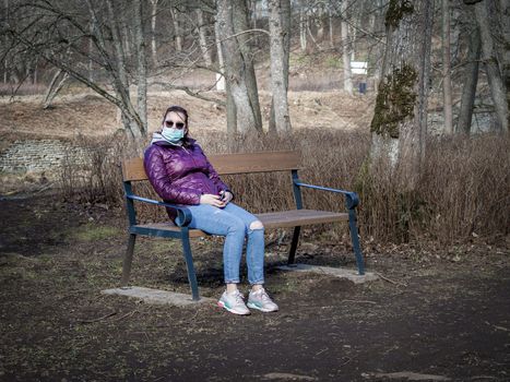 Lady and coronavirus protection. Sad Woman sitting alone on bench in park wearing mask to avoid infectious. Corona virus, or Covid 19, is spreading all over the world. Receives bad news on her phone.
