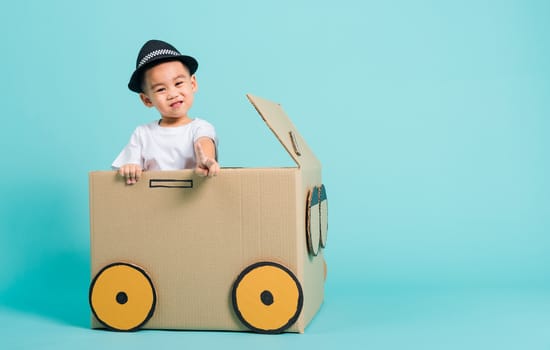 Happy Asian children boy smile in driving play car creative by a cardboard box imagination, summer holiday travel concept, studio shot on blue background with copy space for text