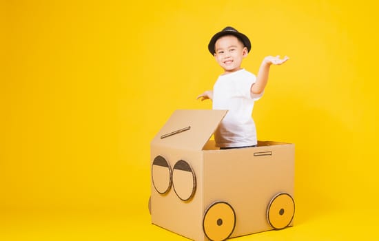 Portrait happy Asian cute little children boy smile so happy wearing white T-shirt driving car creative by cardboard, studio shot on yellow background with copy space