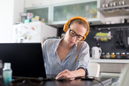 Female freelancer in her casual home clothing working remotly from her dining table in the morning. Home kitchen in the background. Stay healthy and stay at home during corona virus pandemic.