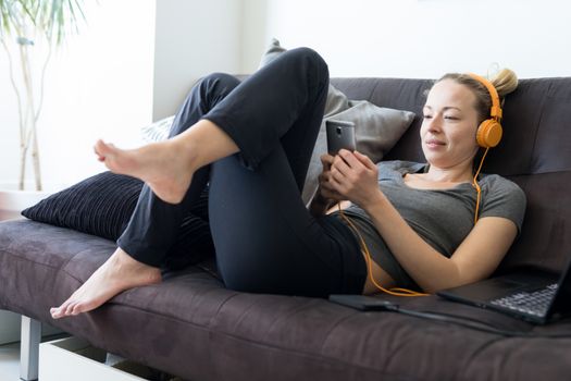Woman in bathrobe being comfortable at her home sofa, using social media apps on phone for video chatting and stying connected with her loved ones. Social distancing. Stay at home.