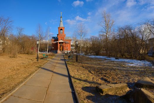 The Orthodox church of red brick surrounded by trees under a blue sky lit by the evening light of the sun in spring.