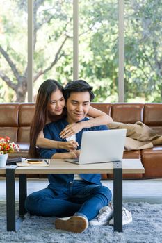 Young lovers spend time together on holidays in the living room. Both of them are interested in internet product information while the man typing keyboard of laptop computer.