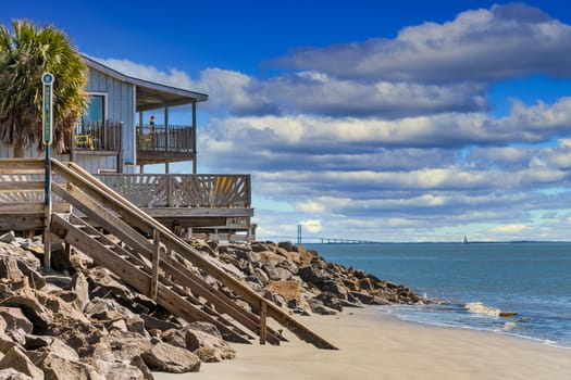 A nice house on the beach with walkway into the sand and a suspension bridge in the background