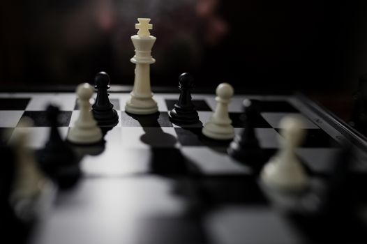 Selective focus of white queen and some black figures on chessboard over dark