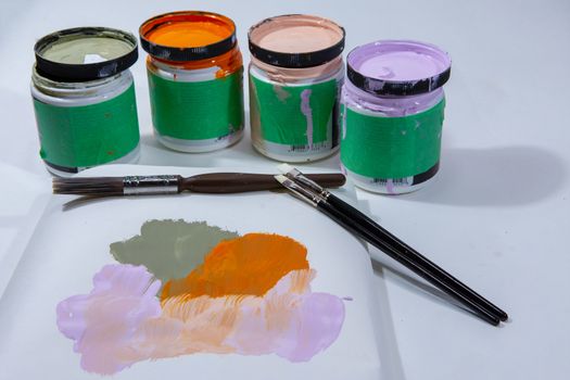 Small cans of paints and brushes on a small piece of white paper for sample color selection