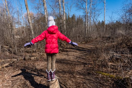 A girl in a spring forest stands on a stump and is about to jump down a path