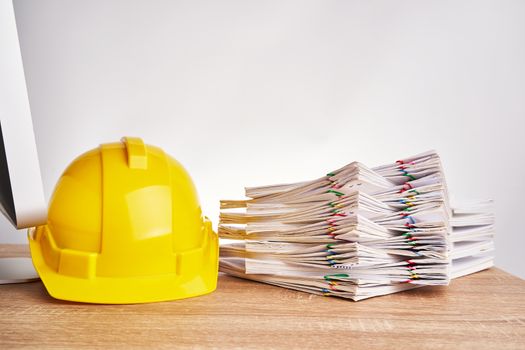 Stack overload document of report and receipt with colorful paperclip with yellow engineer hat on wooden computer table with white background and copy space. Industrial successful concept photography.