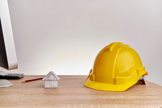 Yellow engineer hat and house  have blur brown pencil and calculator on wooden computer table with white background and copy space. Industrial successful concept photography.