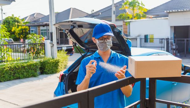 Asian Young delivery man courier online with box in uniform he protective face mask and squirt spray sanitizing, service customer front of house under curfew quarantine pandemic coronavirus COVID-19