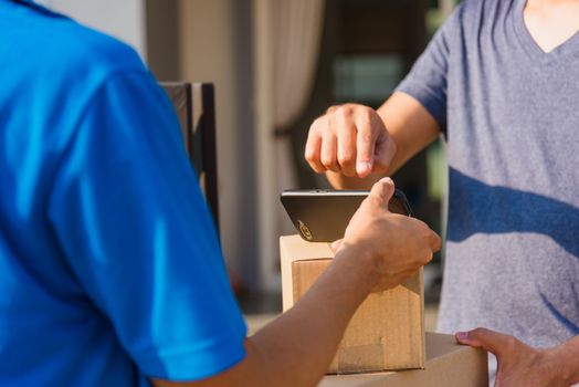 Asian Young delivery man courier shopping online with package post box in uniform he protective face mask he making service and customer using hand finger signature on digital mobile phone at home