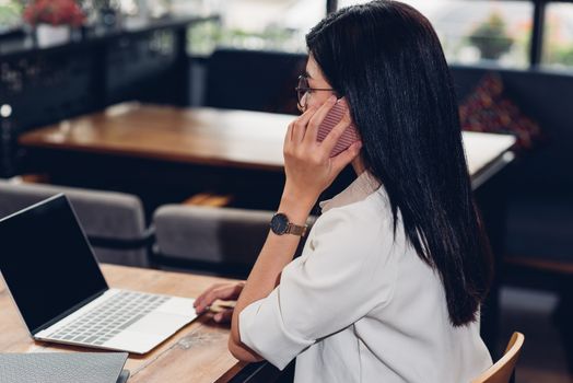 Freelance working woman with laptop computer, he calling smartphone talking with customer in coffee shop