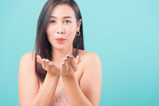 Asian happy portrait beautiful young woman standing smiling blowing something on hands and looking to side on blue background with copy space for text
