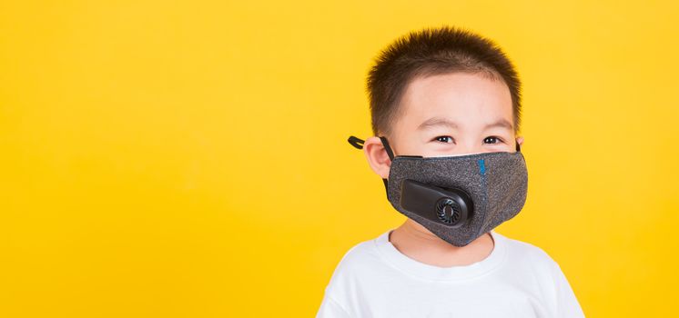 Asian Thai happy portrait cute little cheerful child boy wearing mask protective for covid-19 or pm2.5 dust he looking to camera, studio shot isolated on yellow background with copy space