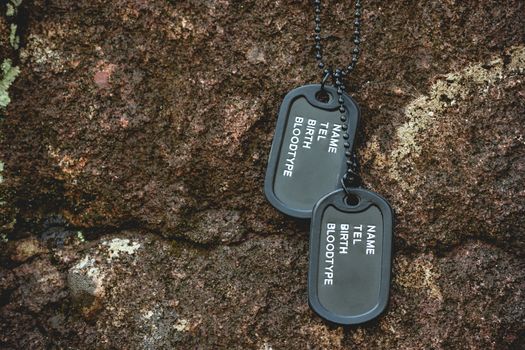 Military tag hanged on the rock on the rock background in forest. Concept of soldier sacrifice and armistice. Closeup and copy space.