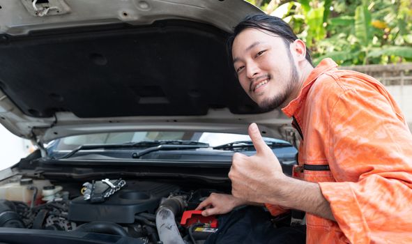 The mechanic in an orange dress uniform opened the car bonnet and discovered an abnormality preventing the car to start. The concept of offsite solution service.