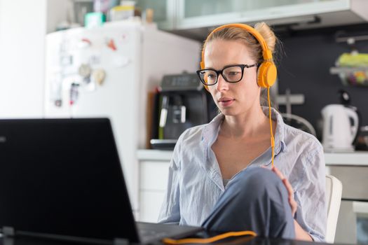 Female freelancer in her casual home clothing working remotly from her dining table in the morning. Home kitchen in the background. Social distancing. Stay at home.