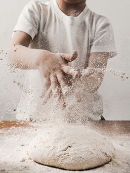 Crop unrecognizable child person clapping hands with flour while cooking bread sprinkling white flour over blob of dough. Vertical. Copy space bottom
