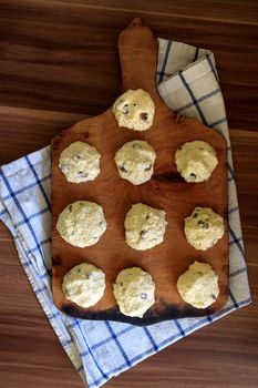 On the board prepared for frying Russian traditional home-made cottage cheese pancakes with raisins - cheesecakes on a wooden table.