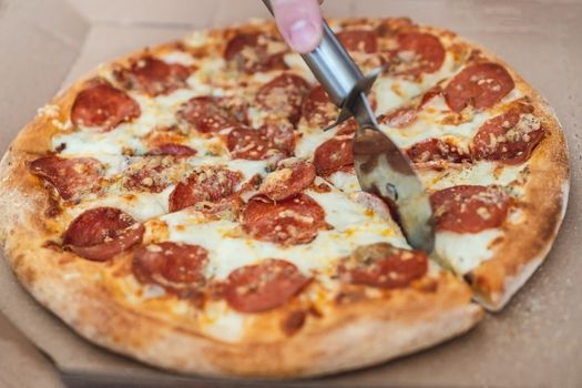 cropped male hand cuts pizza margarita with pepperoni with a special knife, close-up.