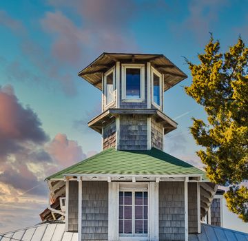 An old cupola on a home under blue skies of wood and green shingles