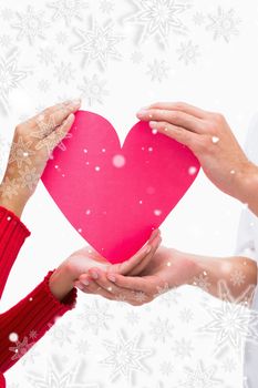 Couples hands holding pink heart against snowflakes