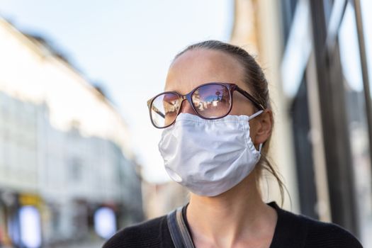 COVID-19 pandemic coronavirus. Young girl in city street wearing face mask protective for spreading of coronavirus disease 2020. Close up of young woman with medical mask on face against SARS-CoV-2.