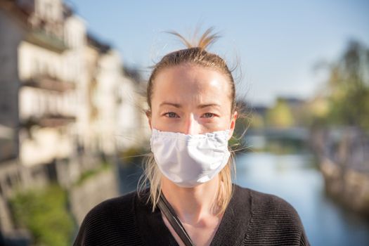 COVID-19 pandemic coronavirus. Young girl in city street wearing face mask protective for spreading of coronavirus disease 2020. Close up of young woman with medical mask on face against SARS-CoV-2.